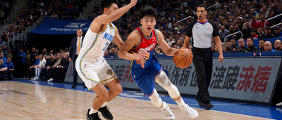 NBA篮球比赛现场，球员运球突破上篮，防守者贴身紧逼，裁判在旁跟进，场边广告牌清晰可见，观众席沸腾